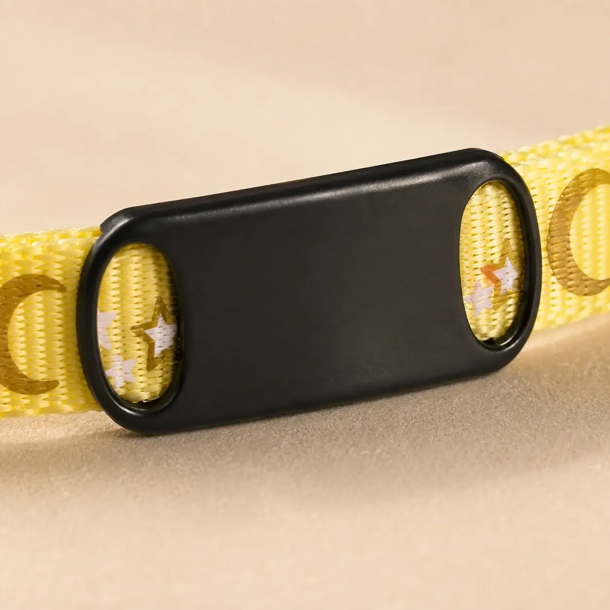 Macro of the black plate slid onto a yellow printed strap, sitting flush with the webbing